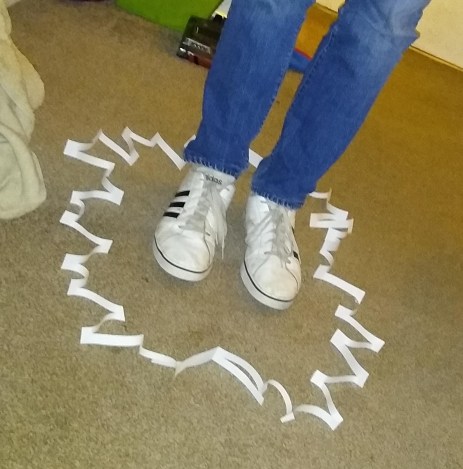 Teenager stood in paper cut up so that you can step through it. In messy living room